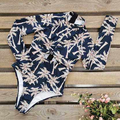 A long -sleeve,one-piece swimsuit with a blue and white palm leaf print and a zipper at the front